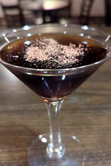A dark cocktail at River’s Edge Supper Club, garnished with cocoa in a martini glass.