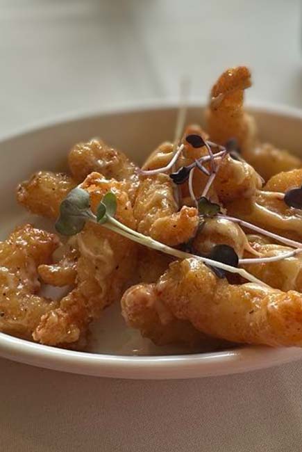 Fried shrimp in a white bowl, garnished with microgreens at River’s Edge Supper Club.