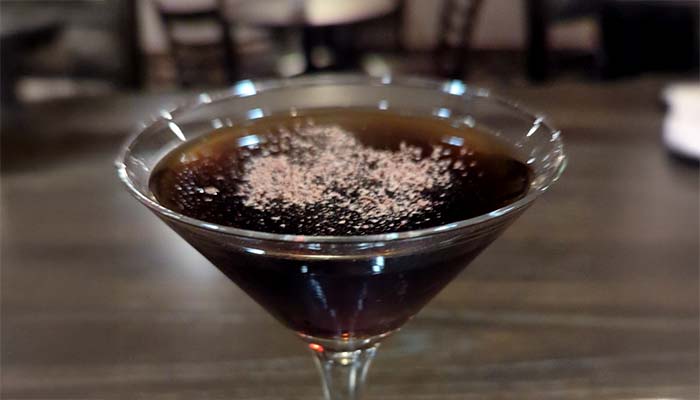A martini glass with a dark cocktail at Marinette Restaurant, topped with chocolate dusting.
