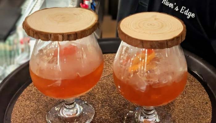 Two cocktails in snifters with wooden lids on a tray at Marinette Restaurant & Bar.