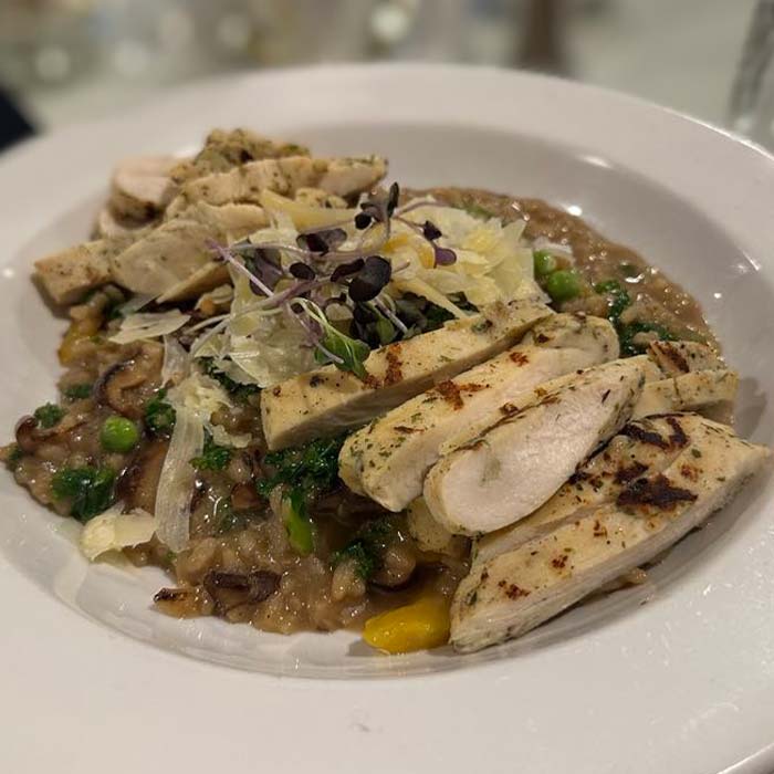 Sliced grilled chicken over creamy risotto with veggies, served at Marinette Restaurant.