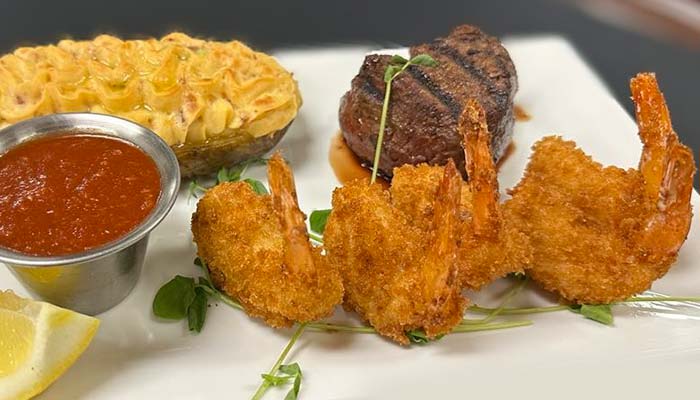 A plate with fried shrimp, steak, twice-baked potato, and cocktail sauce at River’s Edge Supper Club.